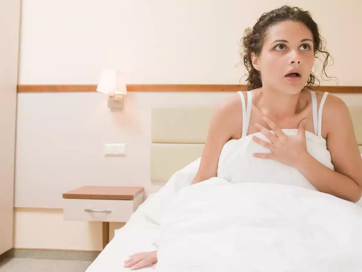 A scared girl sitting on the bed with her hands over her chest